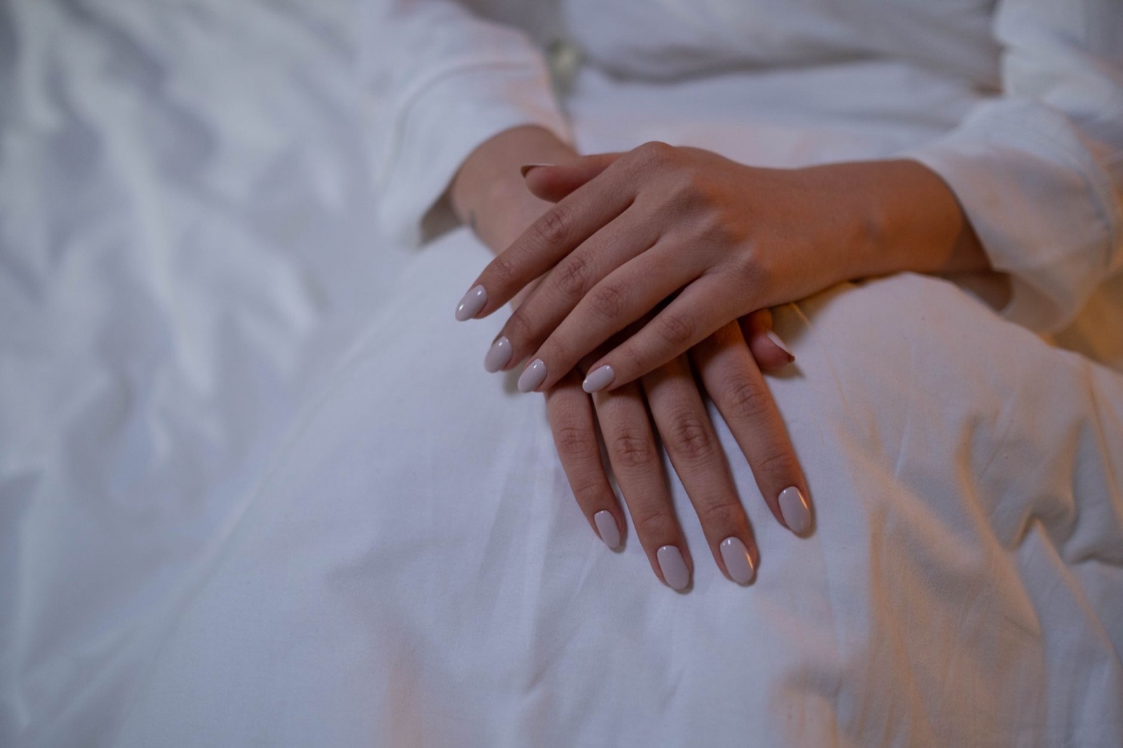 Twee handen met korte, verzorgde nagels in een zachte nudetint op wit linnen