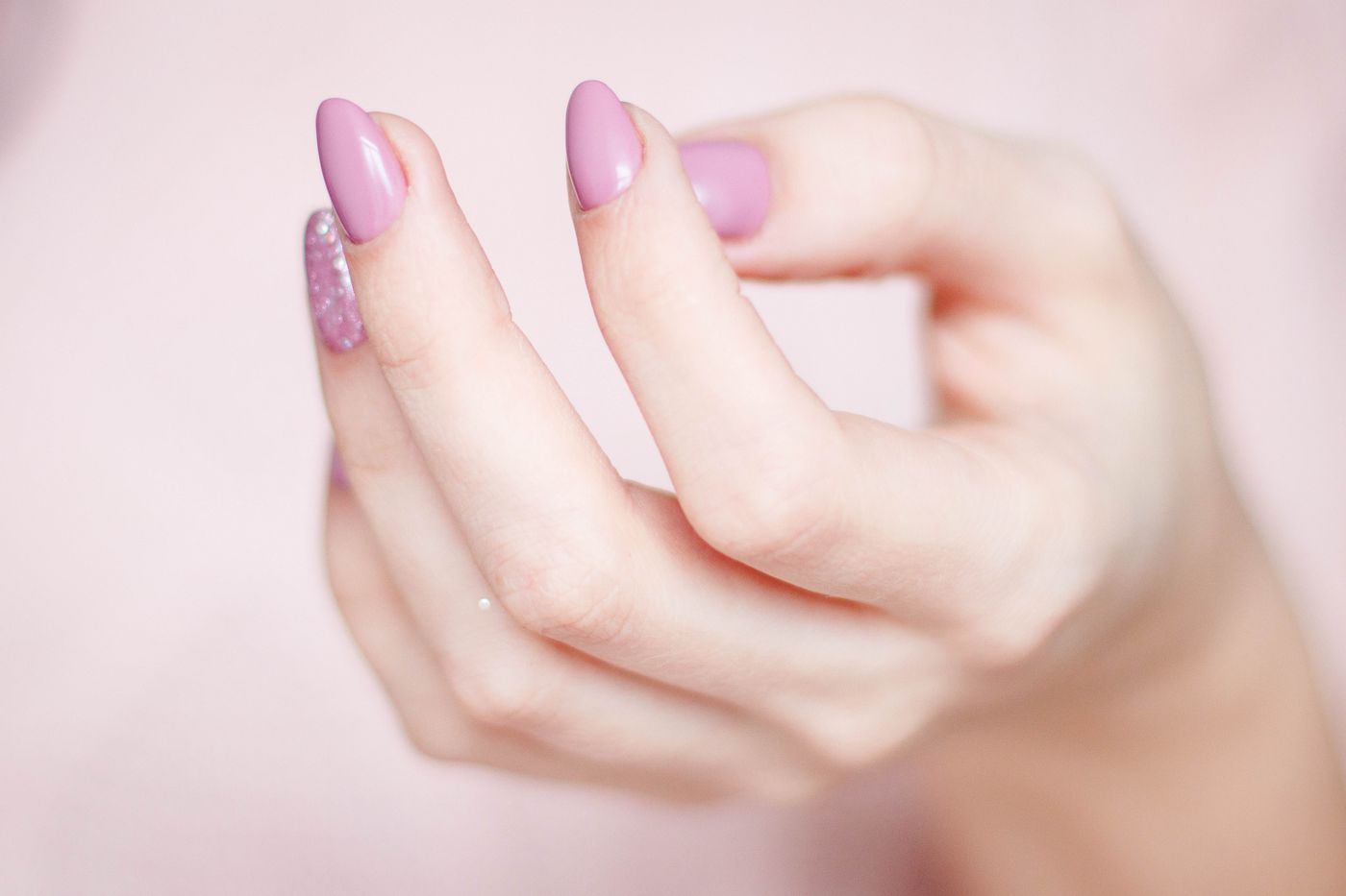 Hand met lila glitternagels tegen een zachtroze achtergrond