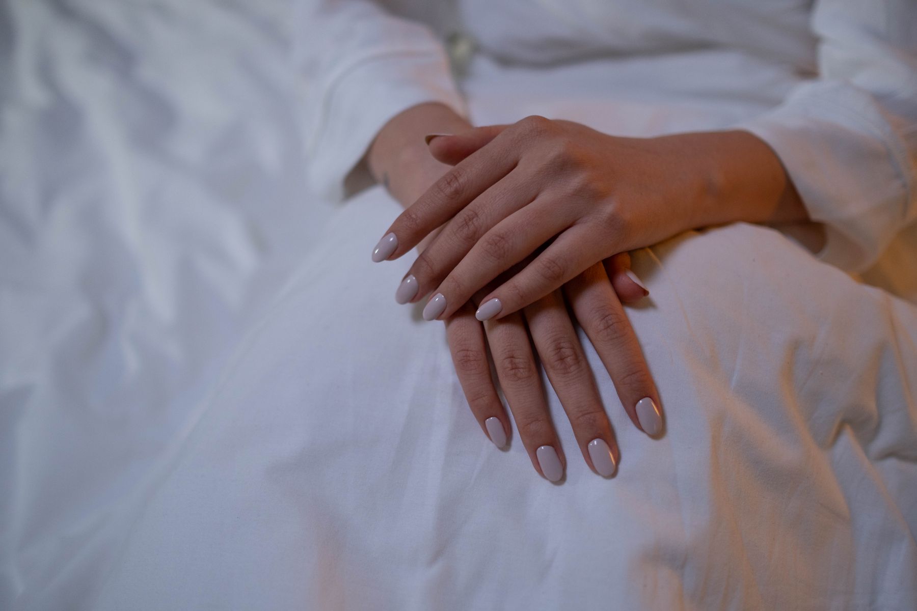Twee handen met verzorgde nude nagels rusten op wit linnen