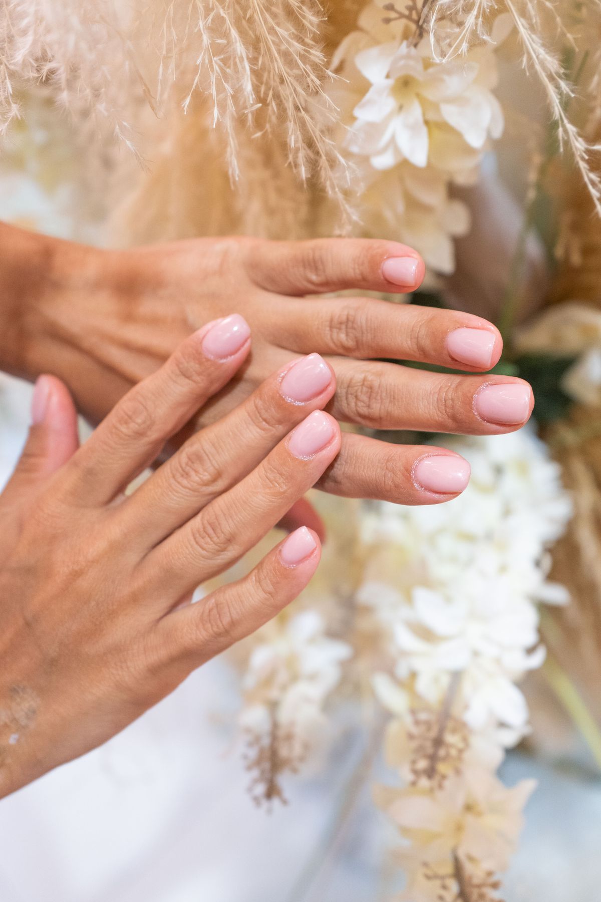 Twee handen met zachtroze, glanzende nagels voor een boeket van gedroogde bloemen en pluimen